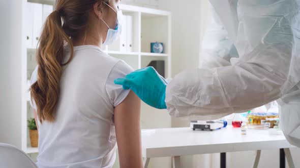 Doctor in Ptotective Costume Making a Vaccine Injection to a Female Patient in a Hospital