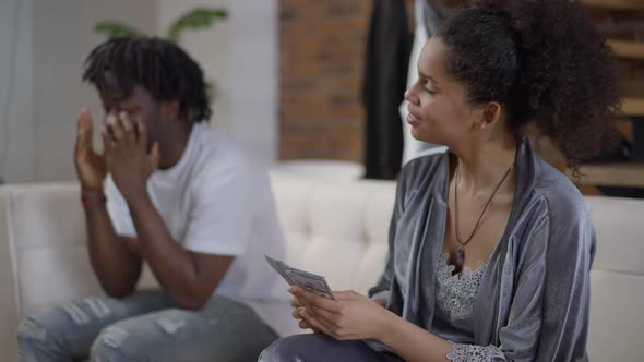 Happy Wealthy Young Woman Admiring Dollars As Frustrated Man Talking Holding Head in Hands at