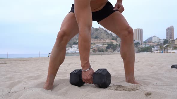 Strong athlete with dumbbell on sand on beach