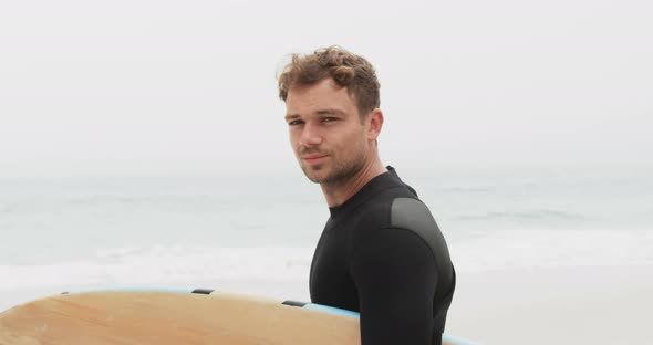 Side view of male surfer standing with surfboard on the beach 4k