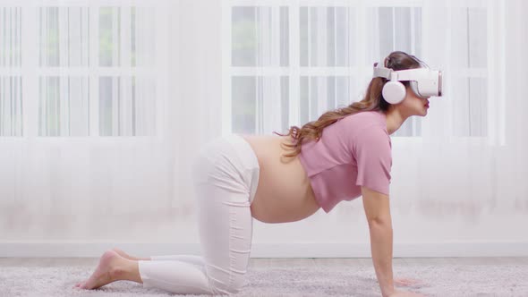 Happy Asian Pregnant woman using virtual reality glasses for practice yoga online class Cat Cow