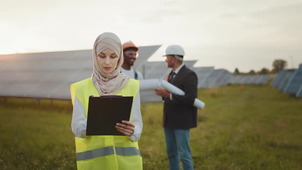 Muslim Woman Hijab Writing on Clipboard While Her Male Colleagues in Helmets