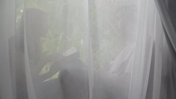 Happy Man and Woman Sitting on the Windowsill Behind the Curtain at Home