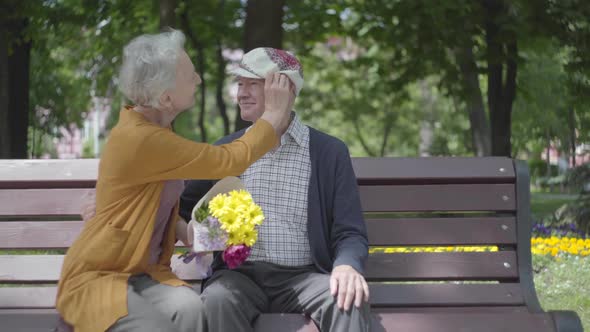 Old Man Kissing His Woman with Flowers on the Banch in a Spring Park