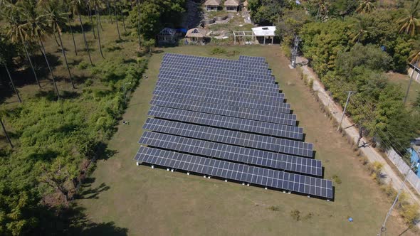 Aerial tilt up shot of solar panel farm field beside palm trees with beautiful landscape in backgrou
