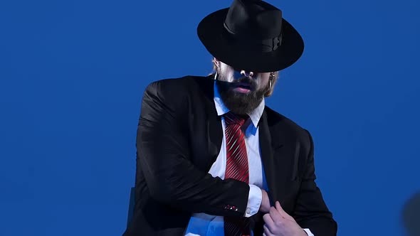 Elegant Man in a Black Hat Is Dancing an Erotic Dance. Spotlight on a Blue Background. Close Up