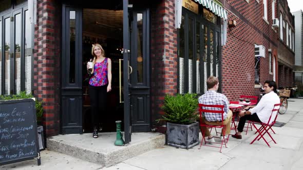 Woman leaving coffee shop, men sitting outdside