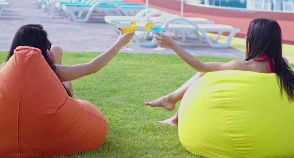 Two Woman Sitting on Beanbag Chairs Near Pool with Drinks