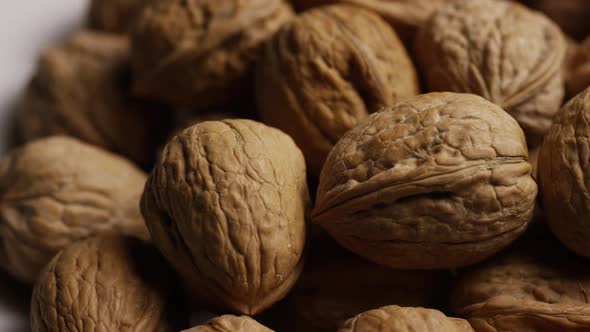 Cinematic, rotating shot of walnuts in their shells on a white surface - WALNUTS