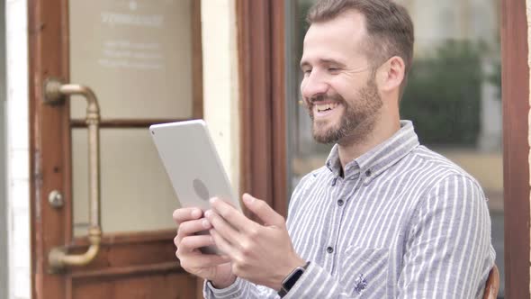 Young Man Watching Video on Tablet While Sitting Outdoor