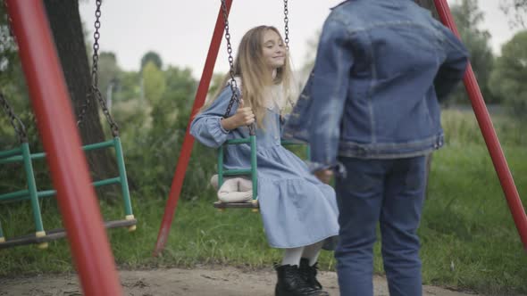 Unrecognizable Schoolboy Giving Bouquet of Flowers To Schoolgirl Swinging on Swings