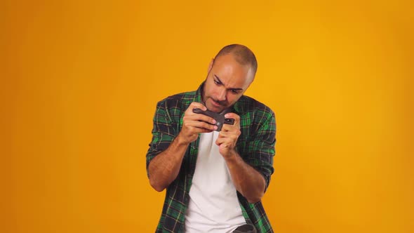 Young African American Man Playing Games on His Smartphone Against Yellow Background