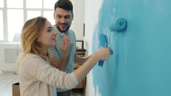 Happy Couple with Paint-covered Noses Kissing and Laughing Painting Wall in Apartment