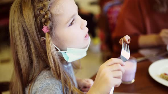 A Little Girl Eats in the Dining Room on the Chin Protective Medical Mask