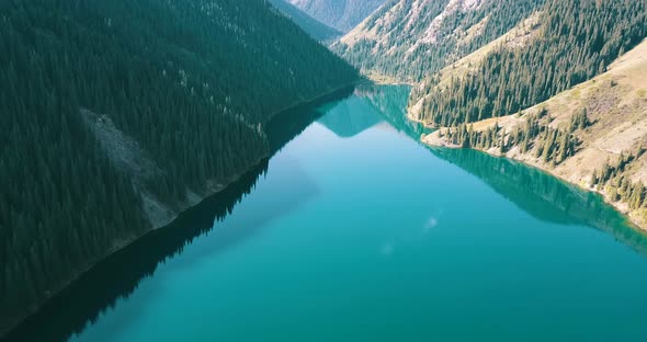 The emerald water of the mountain lake displays coniferous forest, autumn grass, passing clouds.