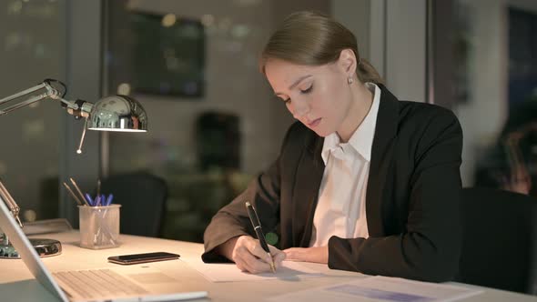 Cheerful Businesswoman Thinking and Writing on Document at Night 