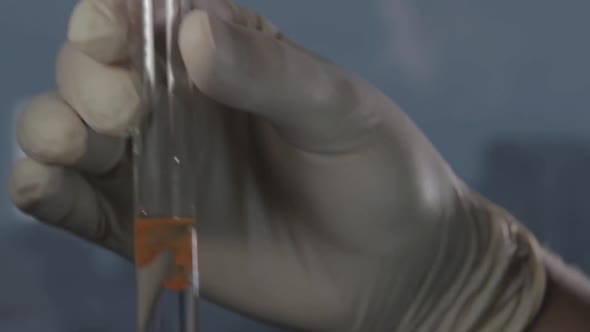 Male Gloved Hand Holding a Test Tube or Glassware with a Clear Liquid.