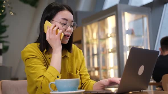 Young Asian Office Worker Sitting at Desk Calling Using Mobile Phone