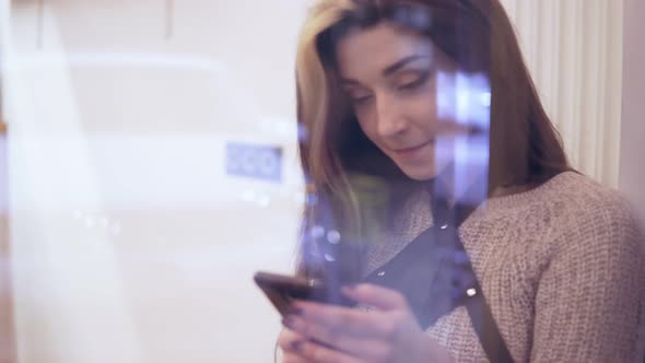 Woman Viewed Through Window with Reflections Using Her Smartphone Chating and Smiling