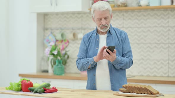 Old Man Using Smartphone While Cutting Vegetables in Kitchen