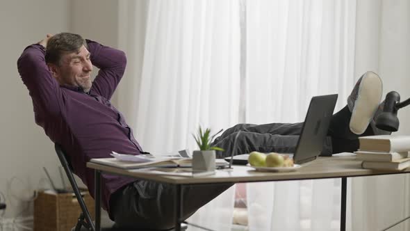 Happy Relaxed Caucasian Man with Feet on Table Talking in Video Chat Smiling and Showing Slippers