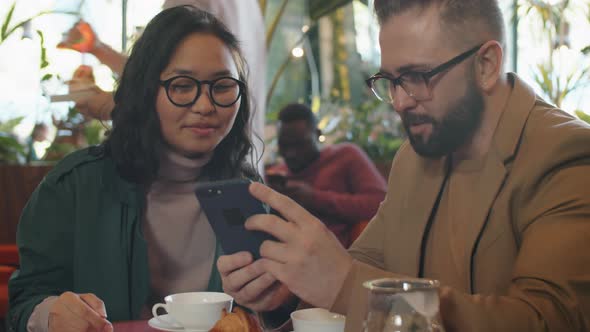 Cheerful Multiethnic Colleagues Using Smartphone and Chatting in Cafe