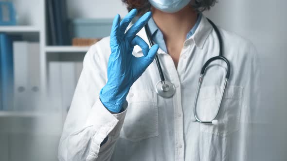 Friendly Female Doctor In White Coat, With Stethoscope In Office. Girl Nurse Shows Ok Sign With Hand