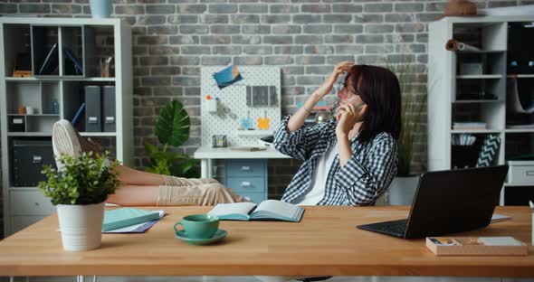 Joyful Employee Chatting on Mobile Phone in Office Sitting at Table Smiling