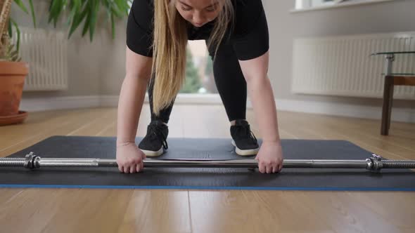 Chubby Caucasian Young Woman Raising Barbell Standing on Exercise Mat at Home
