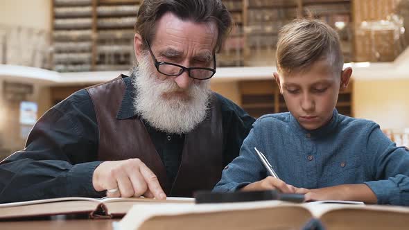 Bearded Grandfather with Handsome Teenage Schoolboy which Reading Book Together in Library