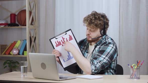Young Man in Checkered Shirt Talking on Video Conference Call Using Laptop and Headset Showing Sales