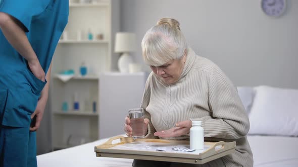 Elderly Female Patient Spilling Water on Tray While Taking Pills, Bad Service