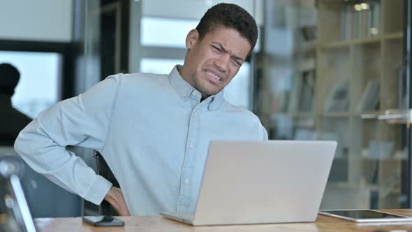 Tired Young African Man Having Back Pain in Modern Office