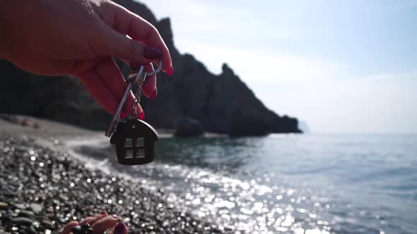 Keys with a Houseshaped Keychain in a Woman's Hand on Sea Beach Background