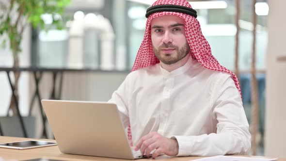 Expressionless Arab Businessman with Laptop Looking at Camera