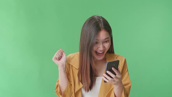 Young Asian Woman Use Mobile Phone, Surprised And Saying Wow In The Green Screen Studio
