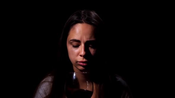 A Tearful and Frightened Sad Girl Looking in the Camera and Drink Wine on Black Background