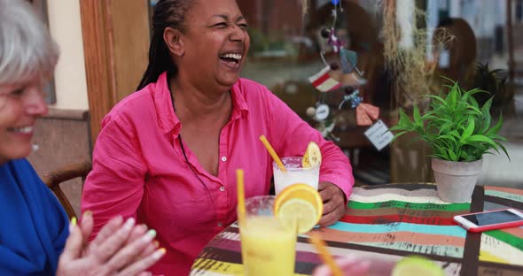 Multiracial senior woman drinking smoothie and having fun at bar outdoor