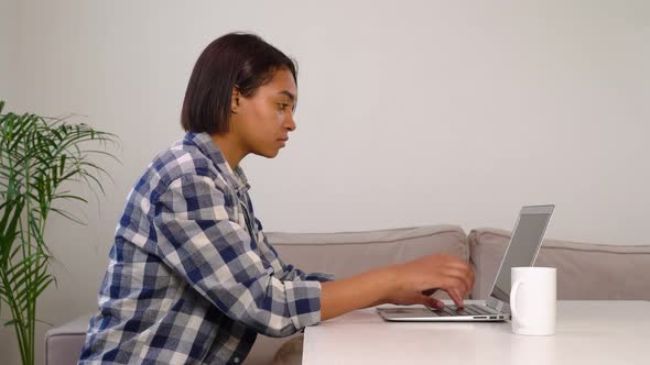 African American Woman Drinks Coffee and Works Online While Sitting at Home