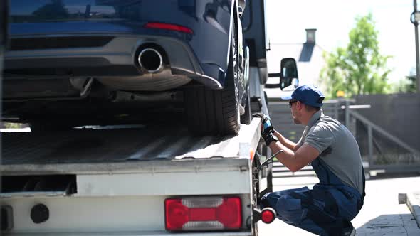 Truck Driver Securing Car On Flatbed Trailer. 