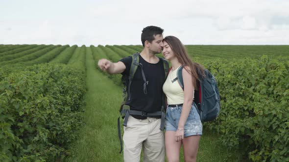 Lovely Couple Walks with Rucksacks and Watching on Currant Plantation