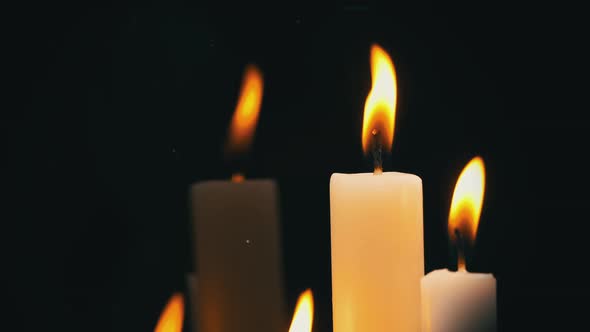 White Paraffin Candles with a Yellow Tint Burn on Black Background in Reflection