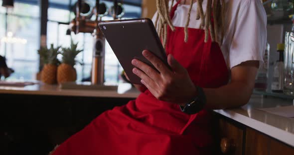 Mixed race male barista with dreadlocks wearing an apron using a digital tablet