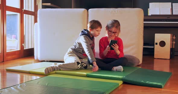 Two Children Playing Together at Home with Smartphone. Brother and Sister Watch Video on Smartphone