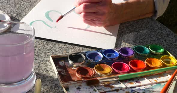 An elderly woman artist painting with vibrant watercolors to relax and release stress in an outdoor