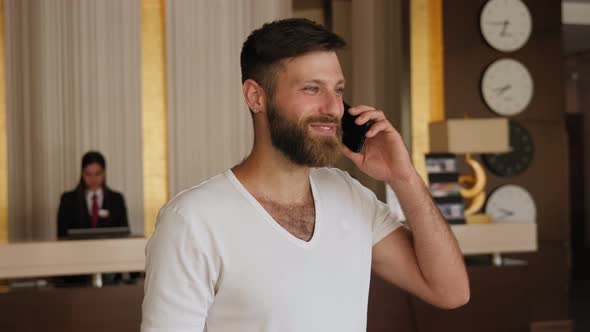 Close-up of a Bearded Man Talking on the Phone in the Hotel Lobby.