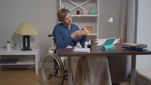 Portrait of Sad Disabled Man in Wheelchair with Vitamins at Home Indoors