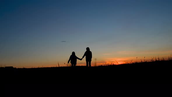 Happy family mom and daughter little girl run through the meadow at sunset.