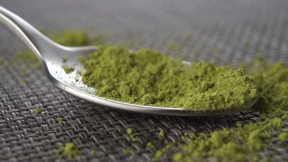 Green matcha tea powder falls into a teaspoon in slow motion