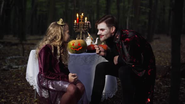 Man with Scary Halloween Face Paint Holding Lollipop Playing with Pretty Girl in Forest in Darkness